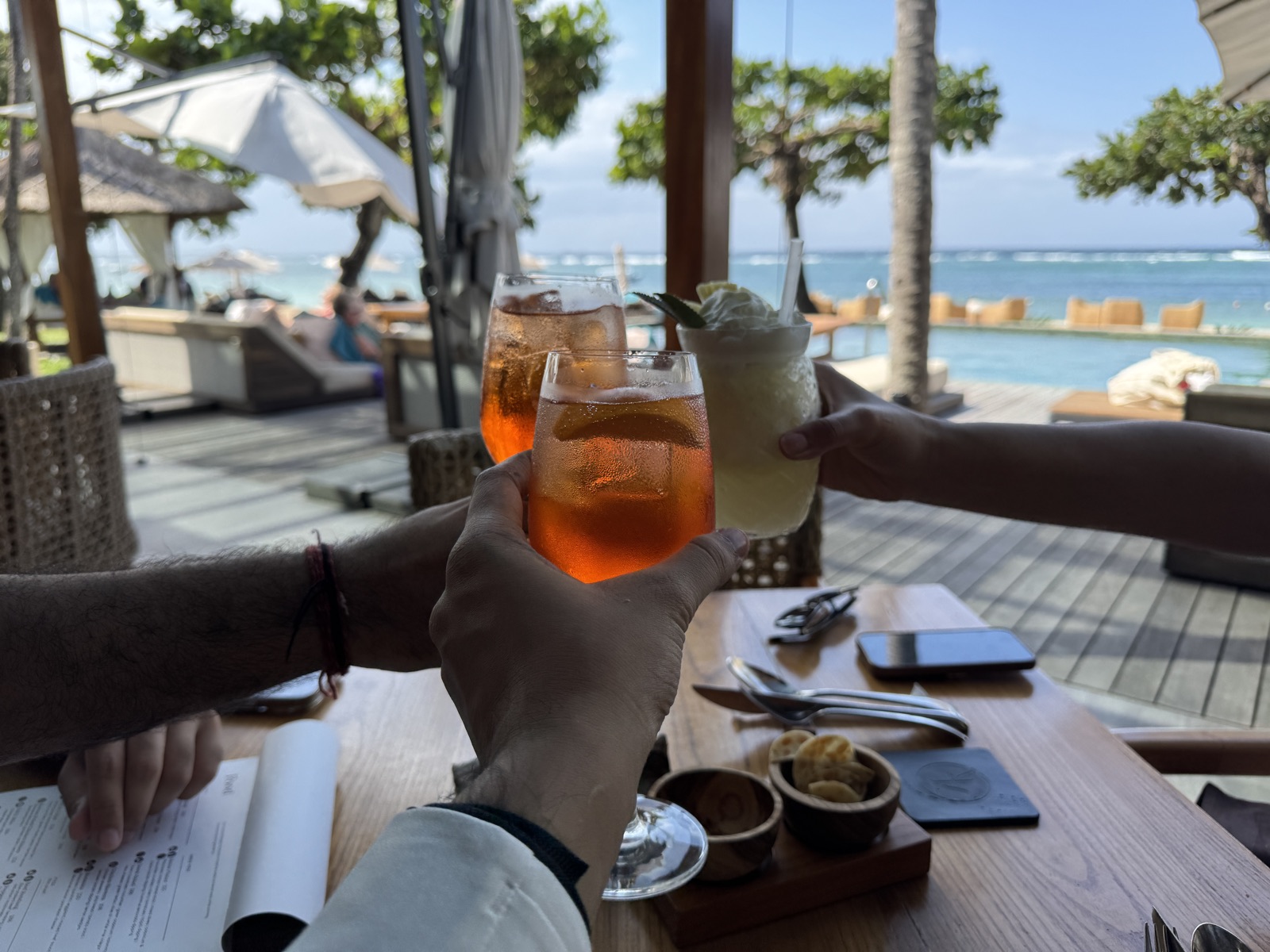 Three cocktails clinked above a beachside table in Bali